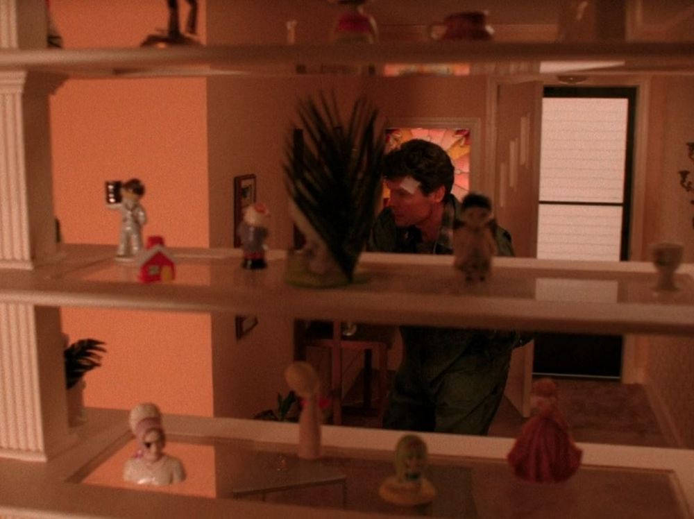 Ed Hurley is coming into his house in Twin Peaks Episode 2. In the foreground are shelves with figurines on them. One of the figurines has an eye patch