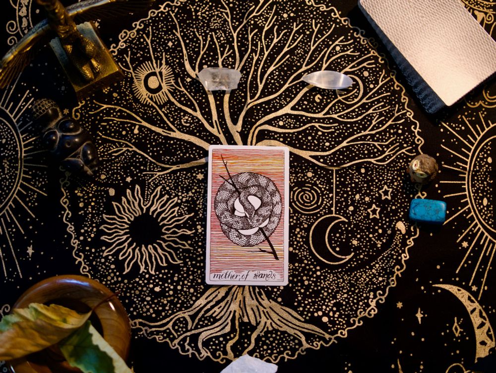 A Mother Of Wands tarot card (a rattlesnake coiled over her eggs and a wand) on a Tree of Life alter cloth with an Isis state a Goddess of Willendorf and assorted stones, leaves and crystals. 