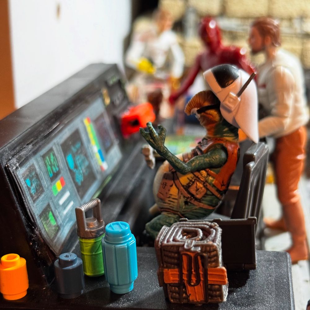 Action figure of Watto wearing a Rebel Fleet Trooper helmet while sitting in front of a control panel 