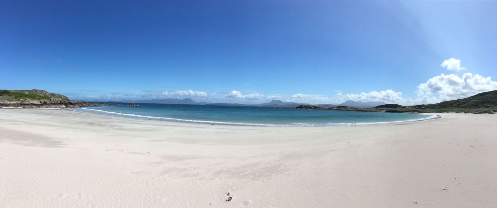 White sand full width of scene. Deep blue sky - a shade only experienced in Scotland.looking out to sea with low level land on either side. White fluffy clouds ( the best type) on the horizon and to the right of picture. 