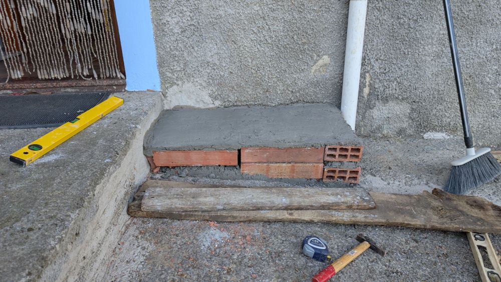 A plinth, about 45 X 80 cm, making a level surface on a concrete slope. The front face is not yet concreted, so you can see the bricks and thick cement to level things up. There are some tools scattered around. 