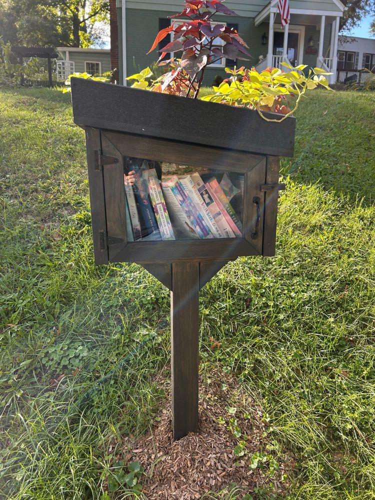 Photo of Little Free Library featuring—wooden post with box on top that holds books.