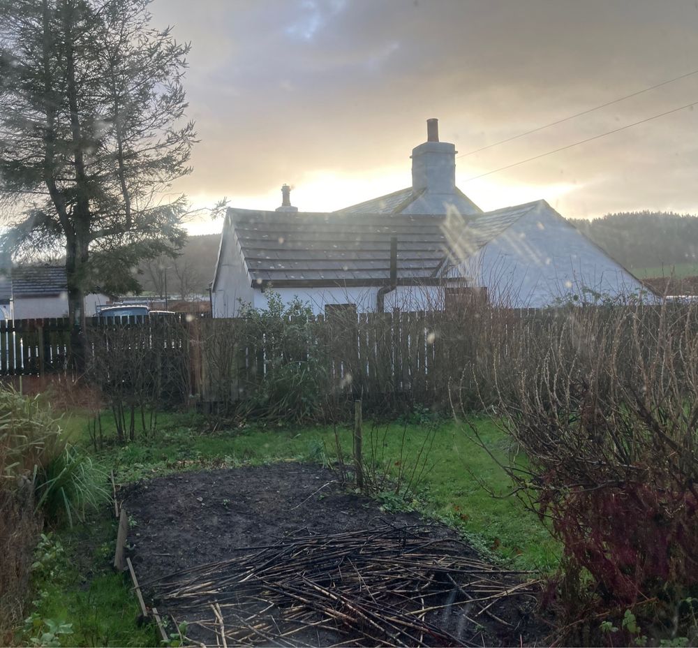 Sun rising over a white stone cottage with a wooded hillside behind