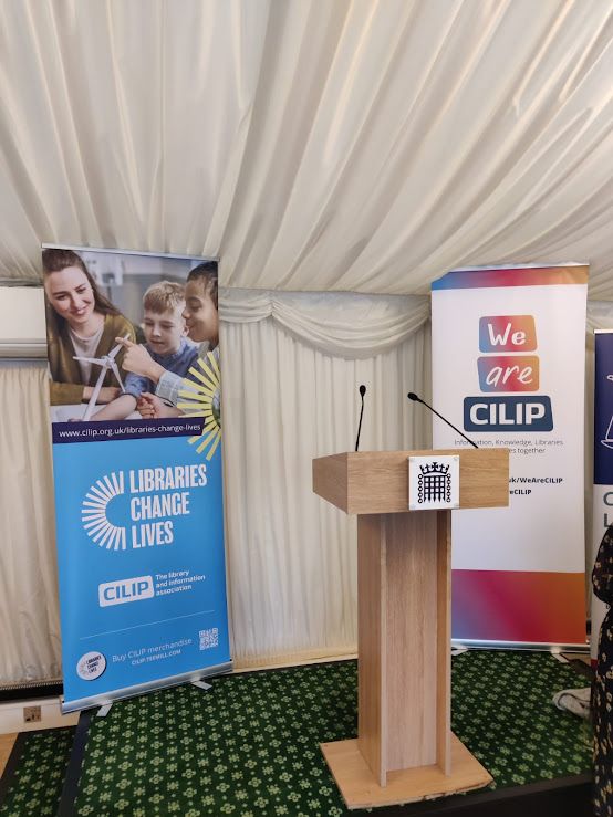 Photograph of a Libraries Change Lives banner and a We Are CILIP banner either side of a House of Commons lectern, in a marquee.