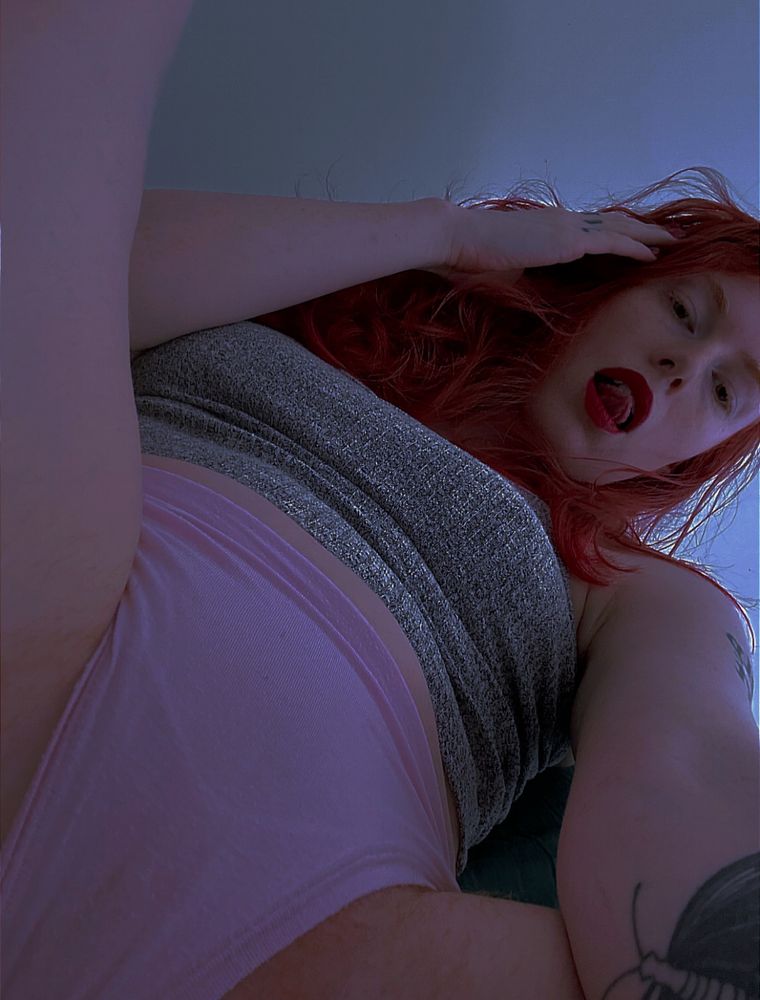 Oh a saucy angle- caught between MissFox’s open legs, pov next to their pink panties, ginger hair fuzzed around it. They reach to the camera, tongue poked up between full, reddened lips.