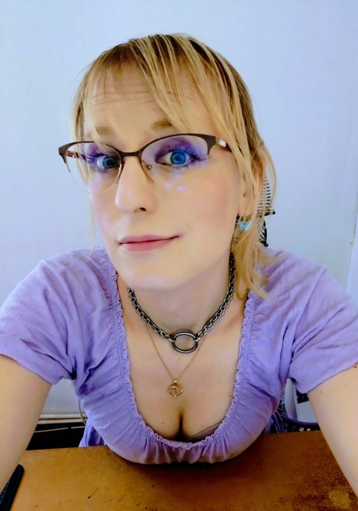 A woman leaning over her desk. Her breasts are resting on top of it. She is wearing a low cut cotton dress.