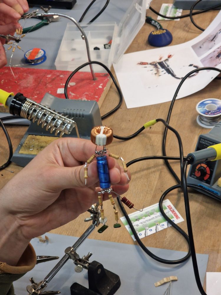 A hand holding a small humanoid figure soldered together out of electronics components