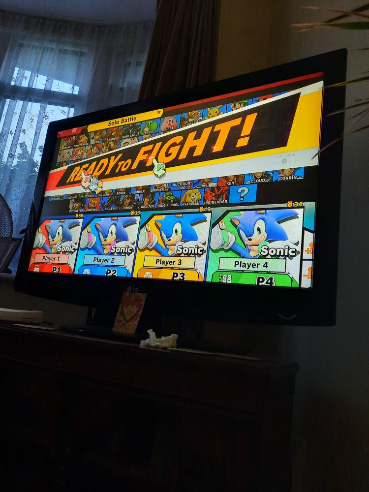 A picture of a TV showing Smash Bros Ultimate withal 4 platers selecting Sonic