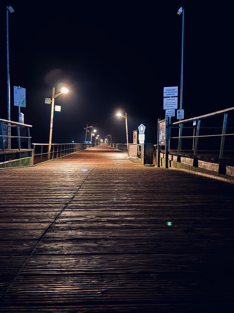 Steg in die Nordsee. Nur Holzboden und ein paar Laternen.  Ende nicht zu erkennen. 