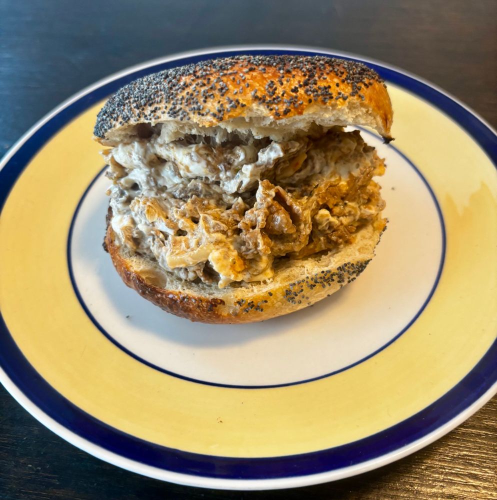 Photo of a poppy seed bagel on a blue and yellow plate with Philly cheesesteak cream cheese