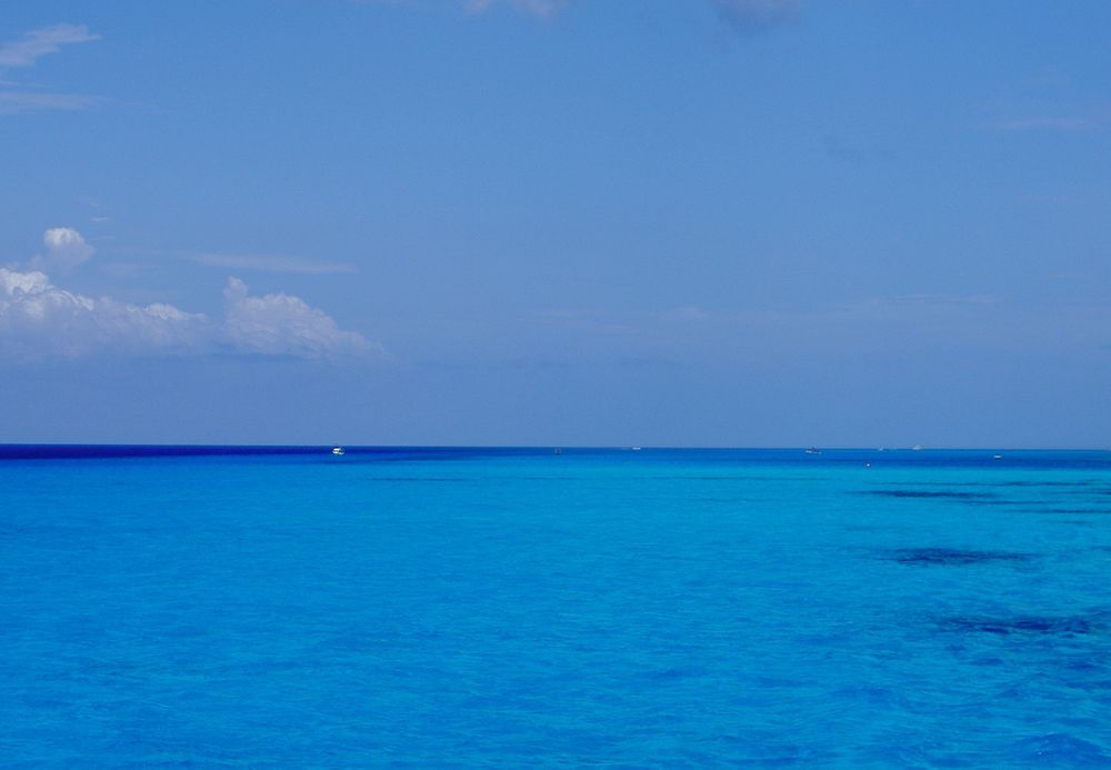 Blue sky with slight clouds over intensely aquamarine water with a deep cobalt blue strip along the horizon. The Gulf of Mexico, as seen off the coast of Mexico.