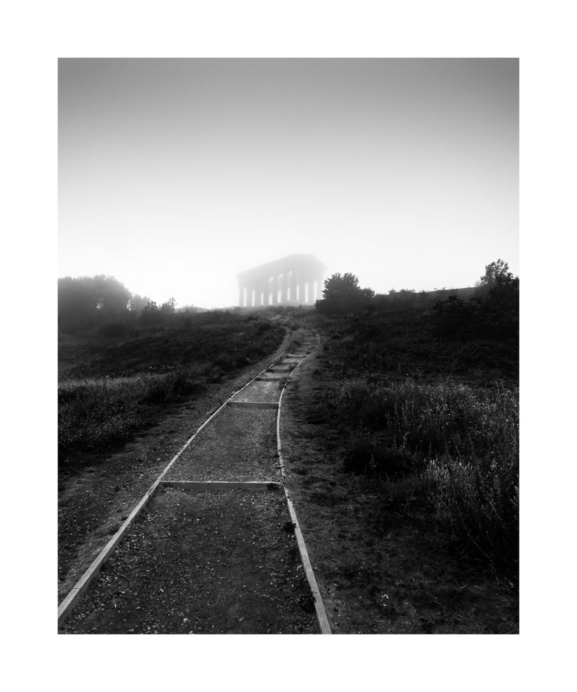 A black and white image with a path leading up to Penshaw Monument which is surrounded by mist  