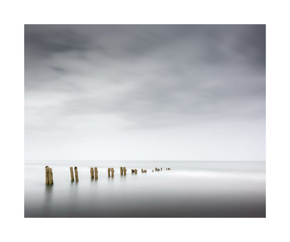 A row of groynes heading into the North Sea with milky cal water surrounding them 