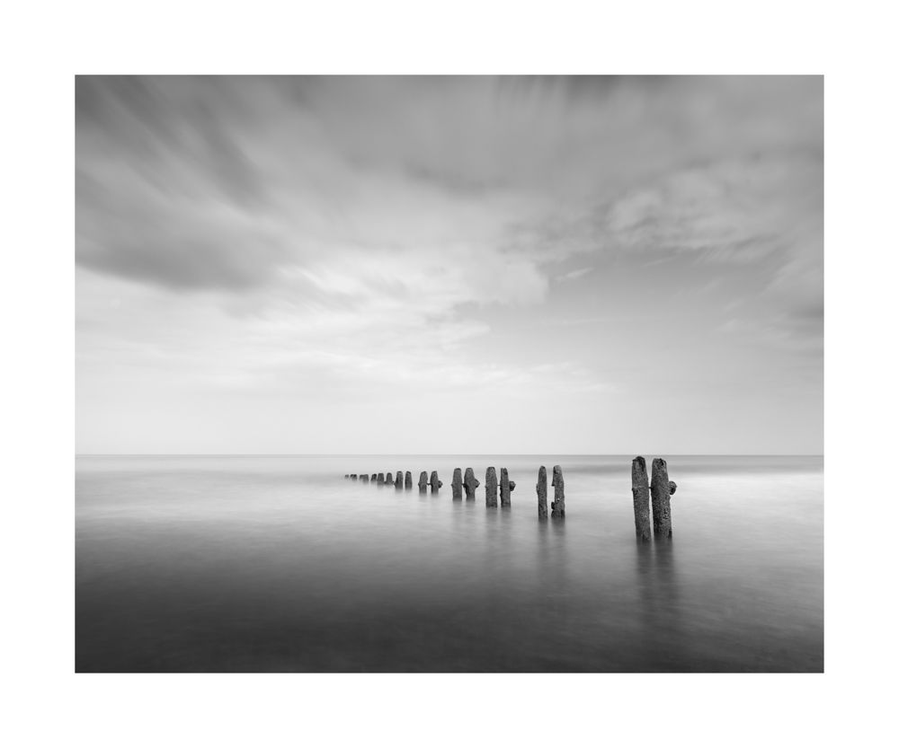 Groynes heading out to sea surrounded by milky calm water