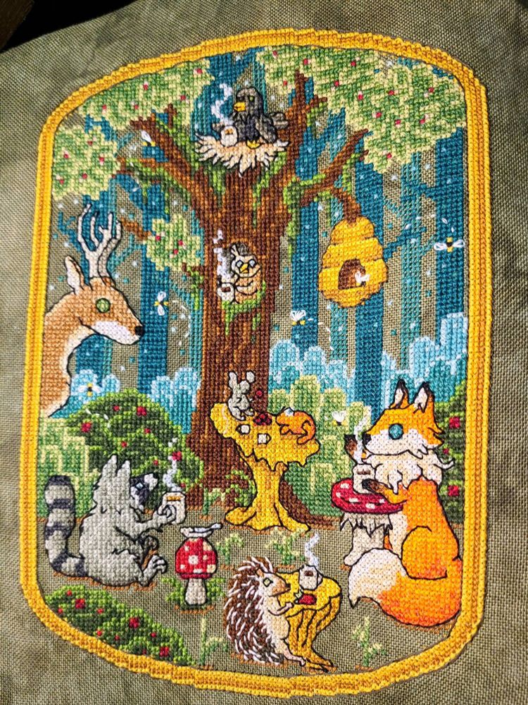 A cross stitch of a forest scene. A variety of animals are gathered having tea. Mushrooms are being used as tables. Steam rises from the tea cups. The forest in the background fades into darker teal trees.