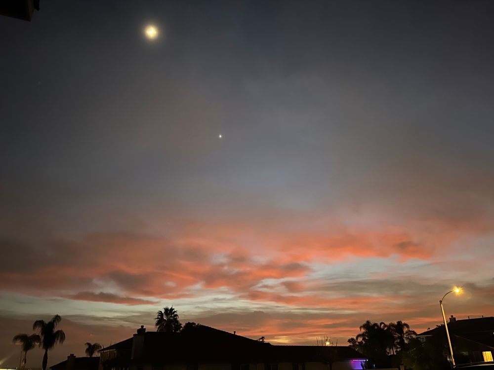 A picture of the clouds in the night sky just after sunset with silhouettes of houses and palm trees underneath.