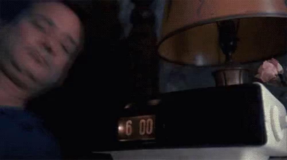 a man is covering his face while looking at a clock that says 6:00 on it