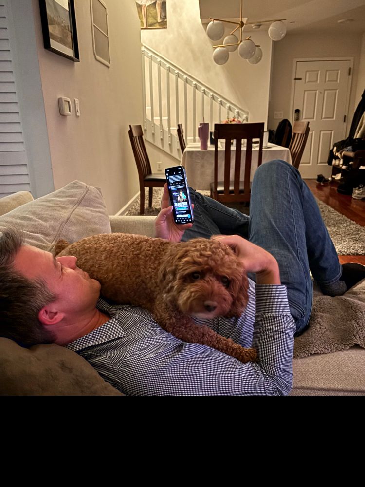 Me Doom scrolling with Bo, our cavapoo resting on my chest. 