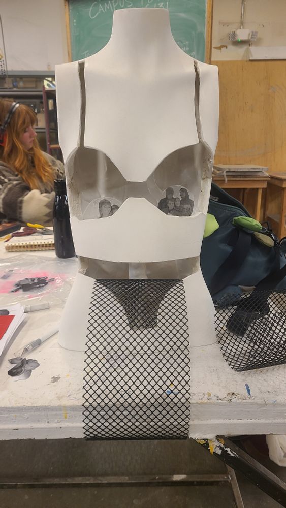 A mannequin torso with a bra and underwear cut out, leaving a hollow inside. There are some photos barely visible inside the bra section and a section of wire sticking out from the underwear cut out like a tongue