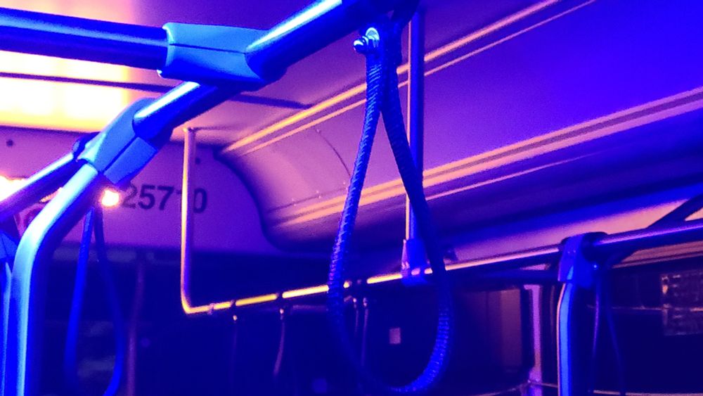 A bus line grab bar is illuminated in blue light from the left and orange light in the back. The colors contrast brightly, creating beautiful hues of purple where they overlap. 