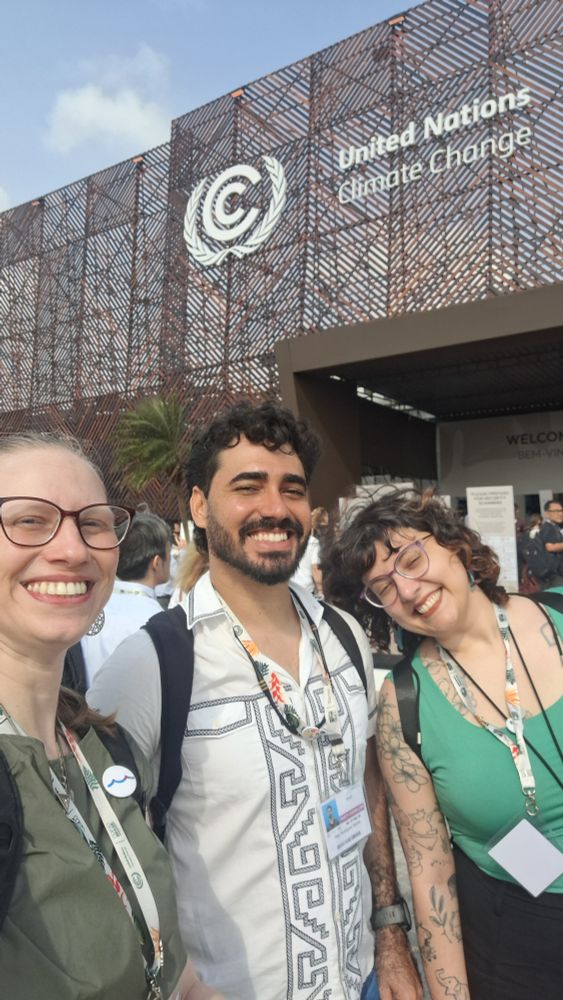 Foto externa. Eu, Yago e Marina com a entrada da COP30 ao fundo.