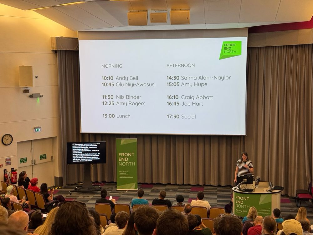 A presenter in a lecture theatre. A small screen is showing live captions of what they are saying