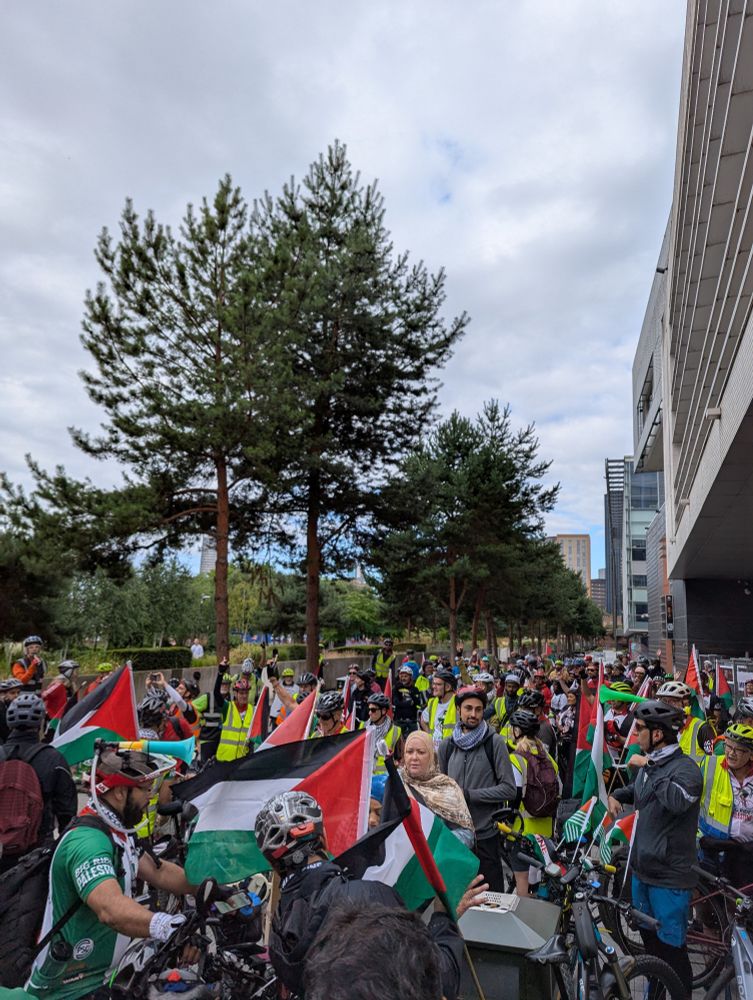 Photograph of a large group of 200 lovely cyclists gathering outside a building with lots of Palestine flags