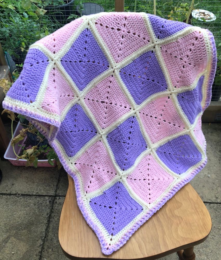 Crochet blanket in pink and purple checkerboard pattern with buttercream connecting each square. The border is a mix of purple and pink.