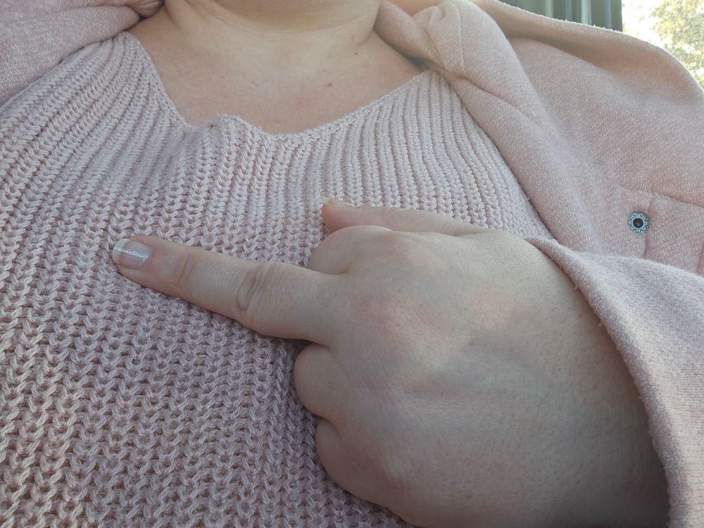 Mein Oberkörper im rosa Wollpulli. Drüber trage ich eine offene, rosa Jacke.
Mittig über der Brust zeige ich meinen Mittelfinger