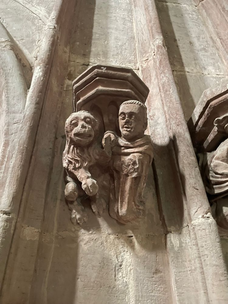 Mittelalterliche Figuren in einer Kirche: ein Affe und ein Mönch, Händchen haltend