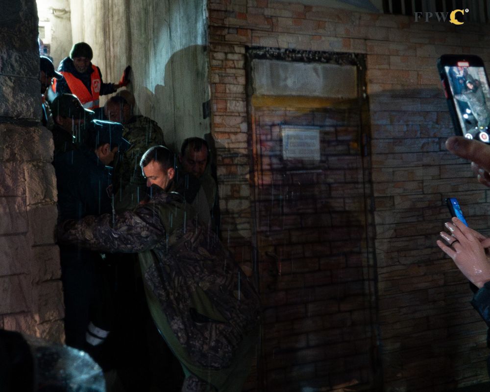 Viele Menschen tragen einen Transportkäfig mit einem betäubten Bären raus auf die verregnete Straße.