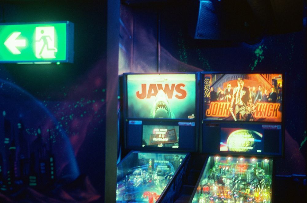 Jaws and John Wick pinball tables behind a glowing exit sign.
