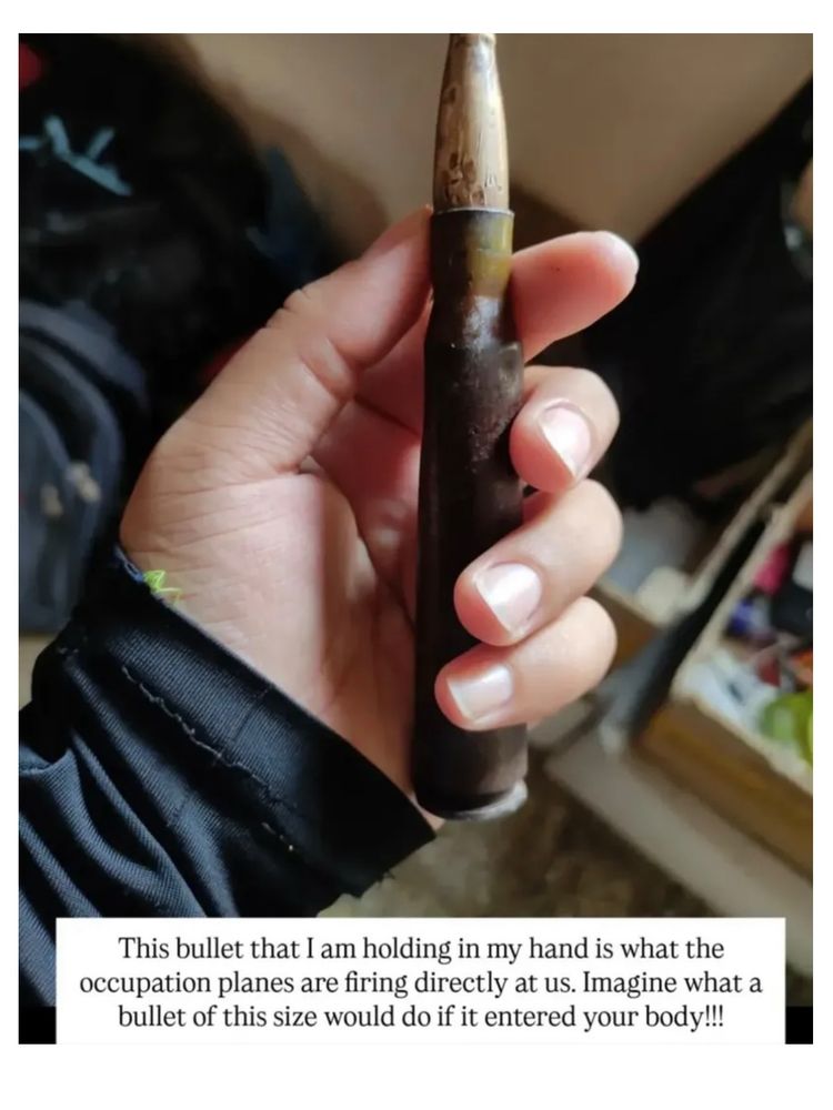 An image of a woman holding a large bullet with the words: "This bullet that I am holding in my hand is what the occupation planes are firing directly at us. Imagine what a bullet of this size would do if it entered your body!"
