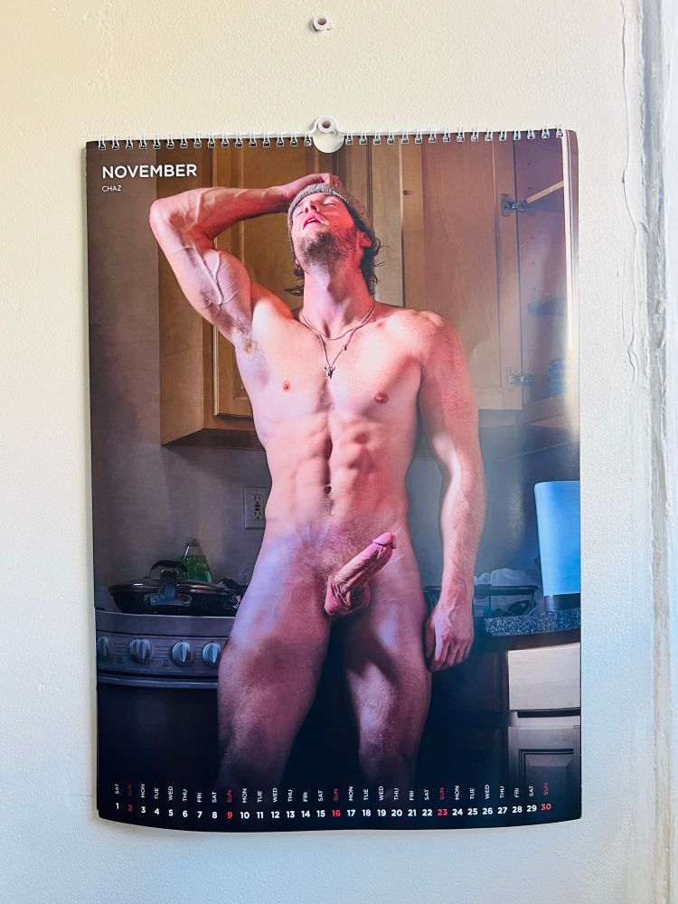 A photo of a white slim and toned man named Chaz in the kitchen standing in front of the driver with his erect cock showing while he flexes his right arm
