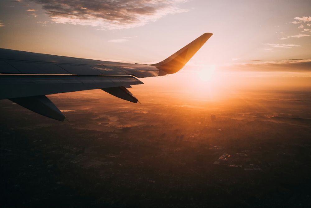 Plane high in the sky with wing of plane in front of a setting sun