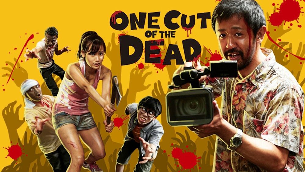 a movie poster for the movie "one cut of the dead." in the foreground, it features a japanese man with scruffy black hair and a beard with blood dripping down his face; he is wearing a hawaiian shirt and holding a video camera. in the background is a younger japanese woman with a ponytail, wearing a tank top and shorts, wielding an access. behind her are three zombies.