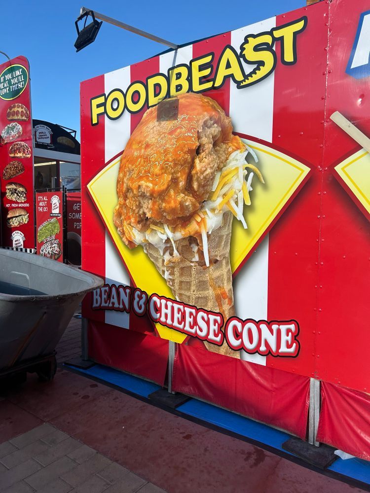 A picture of a carnival food stand - Foodbeast - advertising their Bean & Cheese Cone, which is a scoop of refried beans, plus cheese blend and other contents not visible, in a waffle cone.  Other items can be seen listed, but not clearly enough for inclusion here other than this mention.