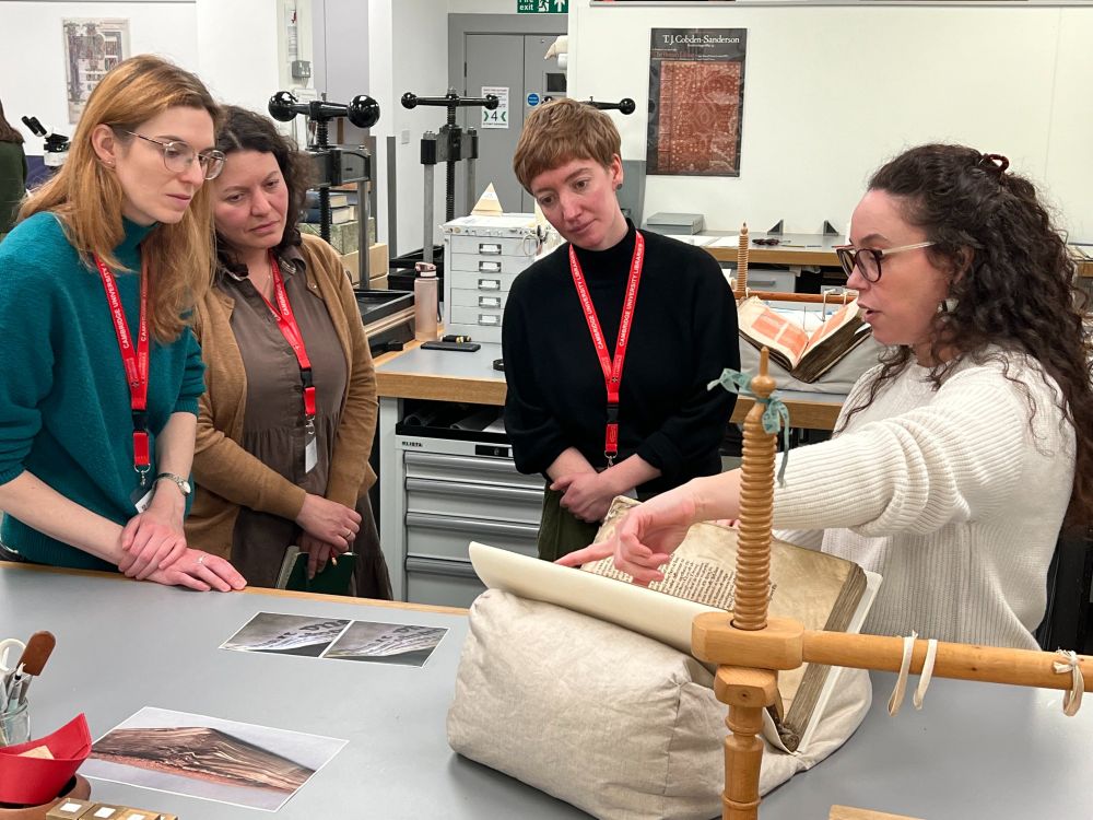 The Cambridge University Library Conservation Department receives a visit from colleagues at the Oxford Conservation Consortium (OCC). We see a group of conservation colleagues looking at an old book in the studio.
