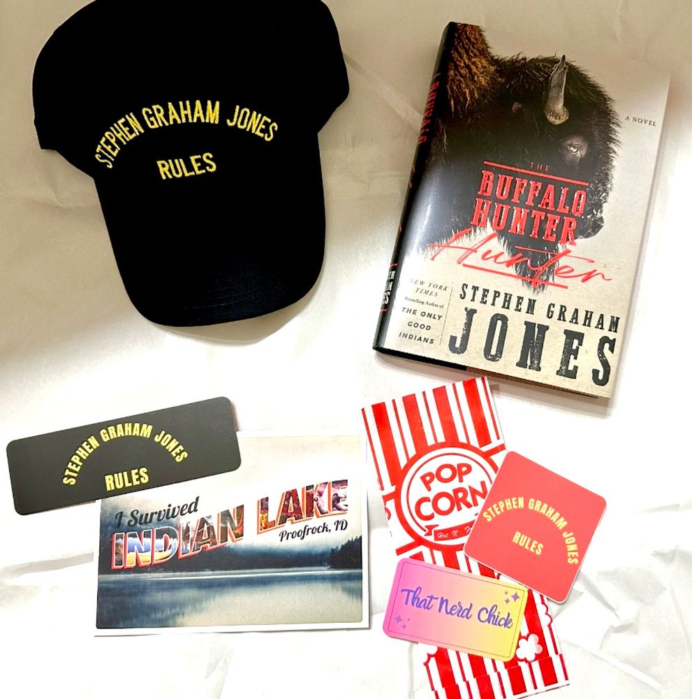 Picture of the oh so cool loot from a giveaway, featuring a Stephen Graham Jones Rules hat and sticker set from thatnerdchick.com and a signed copy of The Buffalo Hunter Hunter by Stephen Graham Jones and an "I Survived Indian Lake Proofrock, ID" postcard. 