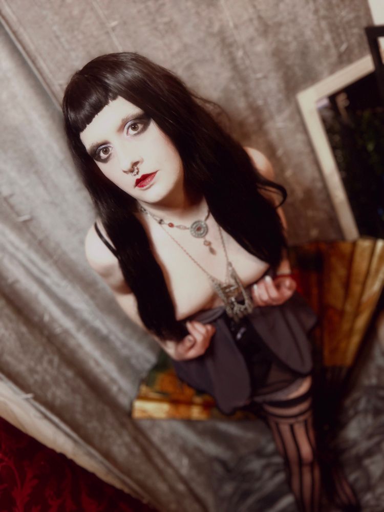 Gothic Boudoir photo of a woman with long black hair, in stockings. Bending over with her dress pulled, exposing her breasts hidden behind her hair.