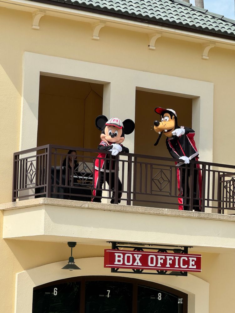 Mickey and Goofy in their sports outfits welcoming guests from a balcony 