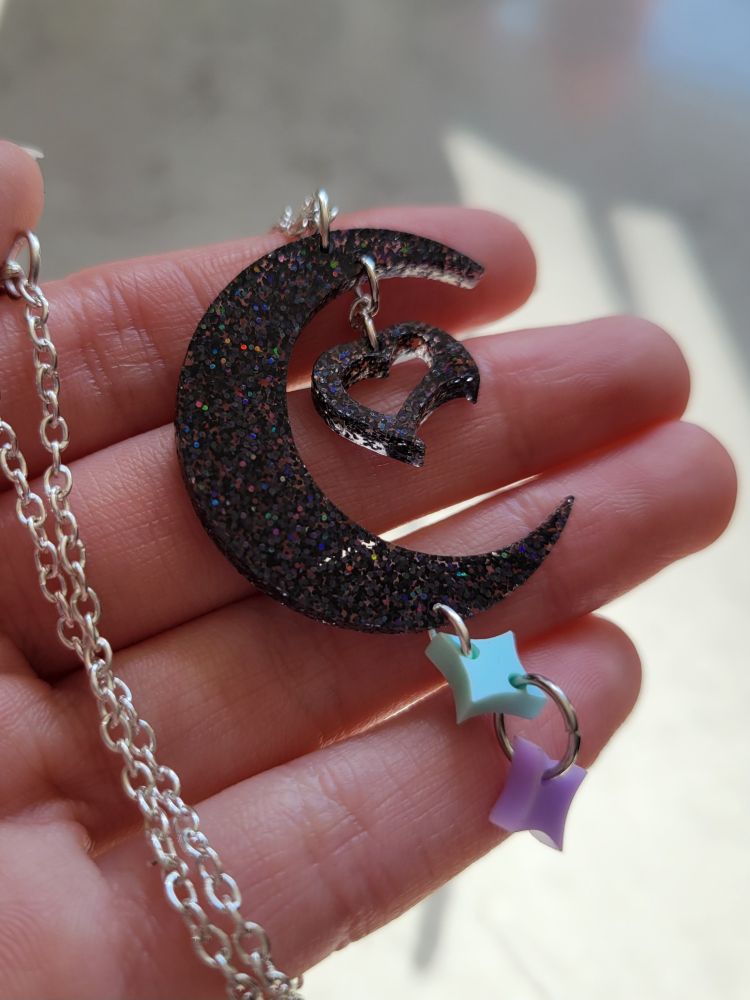 A necklace inspired by Fasunate's brand design. It had a crescent moon with a curvy, stylized heart in the middle made with glittery acrylic material; and mint-colored and lavender-colored stars that hang below.