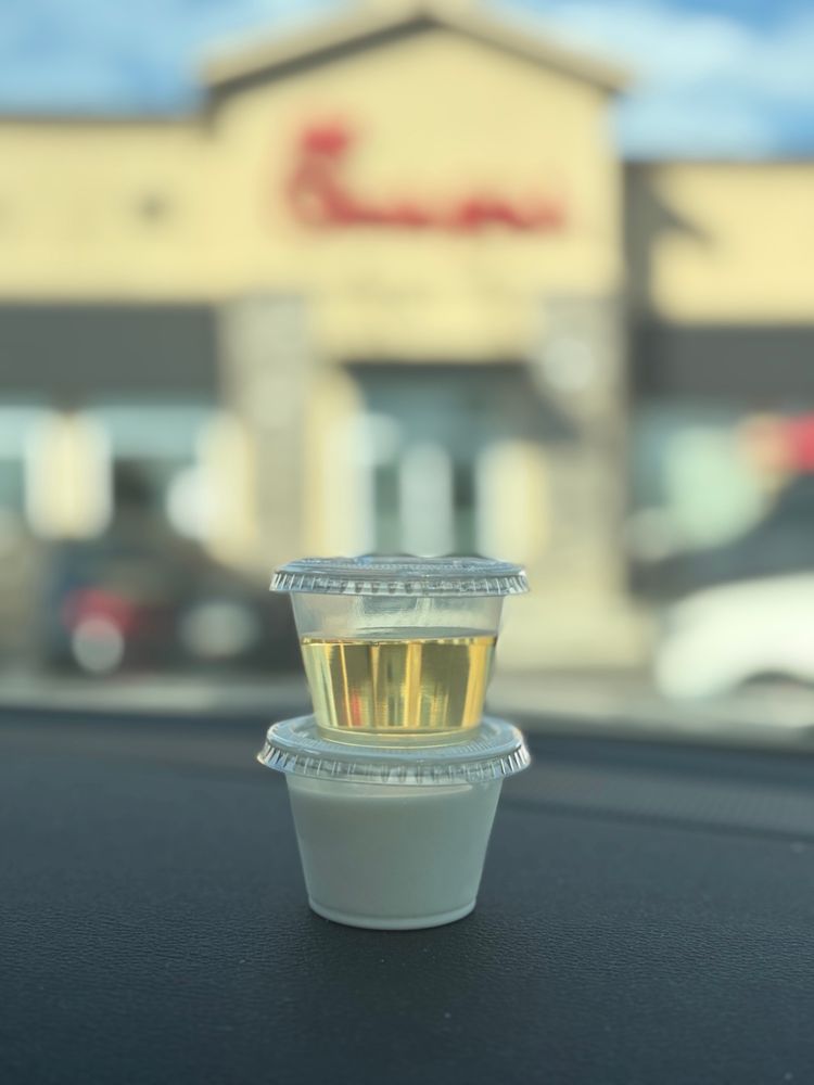Picture of two clear Togo sauce cups with lids stacked, the bottom filled with half and half, the top one filled with a yellow oil (apparently vanilla flavoring pumps) sitting on a dashboard, a blurry Chickfila sign in the distance. Absent: anything to stir with.