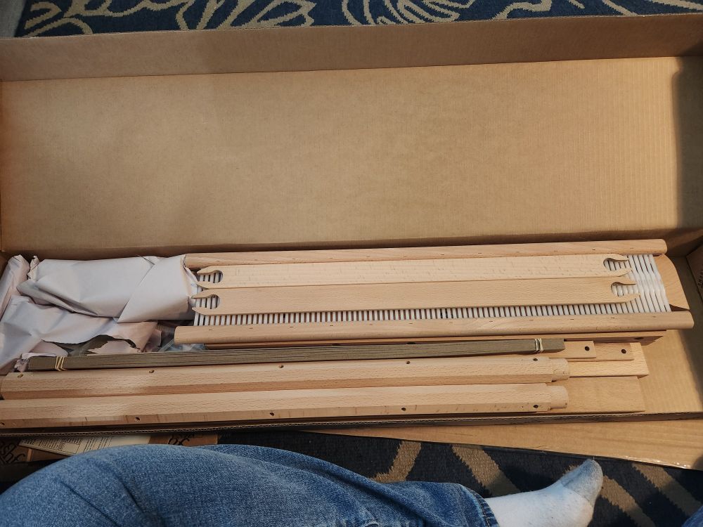 A picture of an unassembled rigid heddle loom in a box on the floor