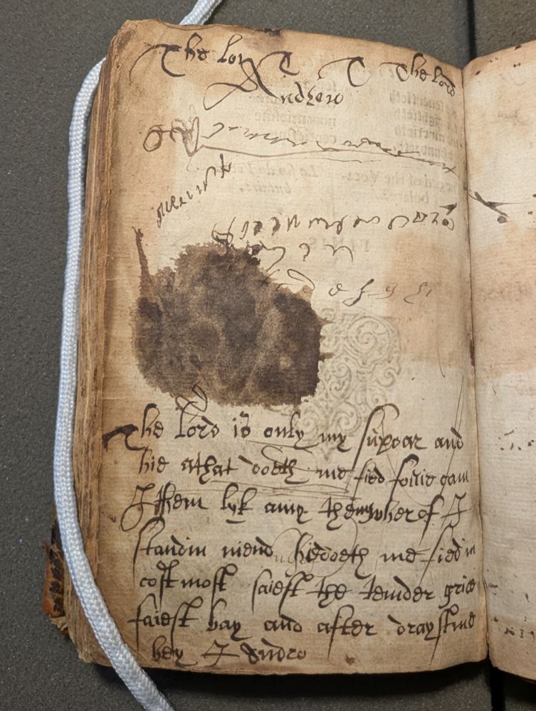 A page busy with inscriptions! Some names, a prayer, pen trials, a big old stain. 