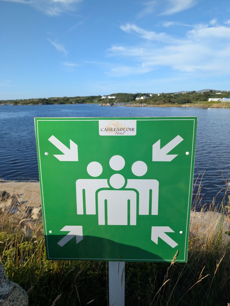 A green warning sign with four arrows, one in each corner, each pointing towards a group of four human figures arranged like the lads in the Bohemian Rhapsody video. 