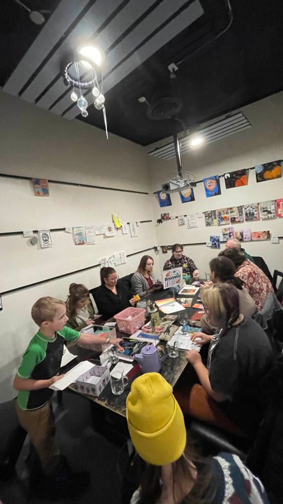 People gathered around a table creating zines for fun, no profit in mind, just relaxing in community 