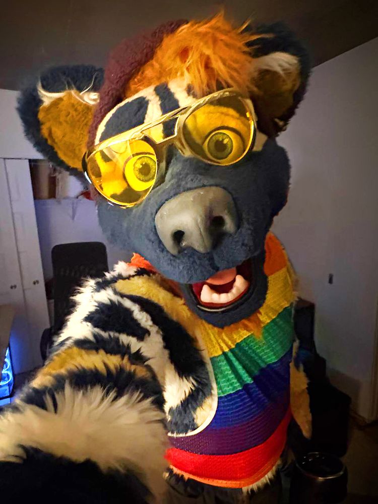 A dog fursuiter taking a selfie while wearing yellow sunglasses and a rainbow shirt