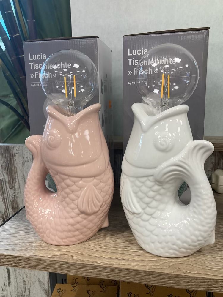 Two tabletop lamps in fish shapes on a store shelf. A pink and a white fish that look up and hold a retro light bulb as their lamp lights in their mouths. They look a lot like a ceramic vase I own but they’re sold as functioning lamps, unclear if the designer had the Simpsons joke in mind.
