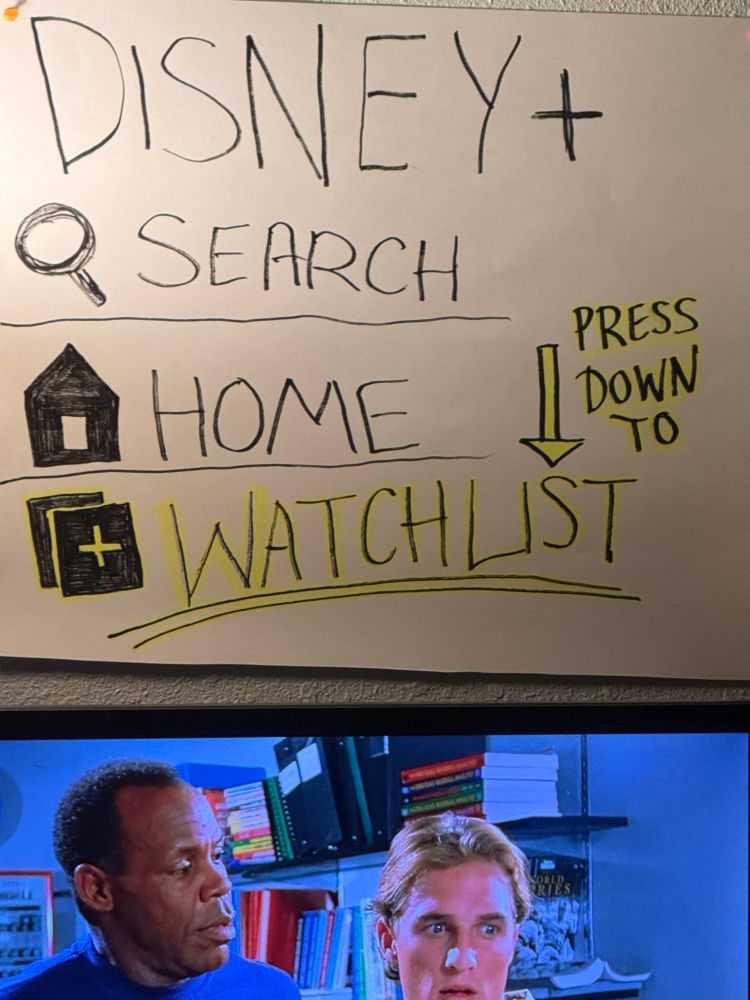 Above a tv is a homemade poster with instructions on how to get to the watchlist in the menu on disney+ in large print with symbols and highlighting. 